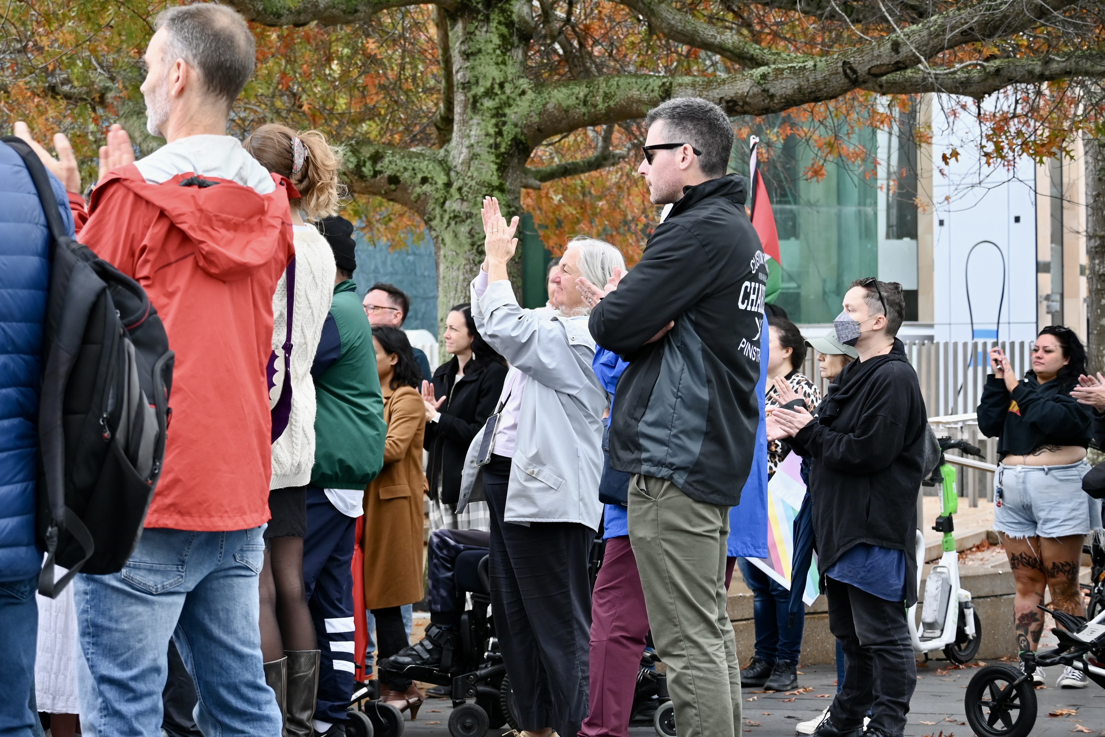 A crowd gathers at a protest rally. A woman stands in the middle raising and clapping her hands.