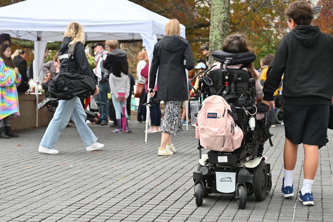 A young person in a powered-wheelchair and another young person head towards a crowd of people at a protest rally. 