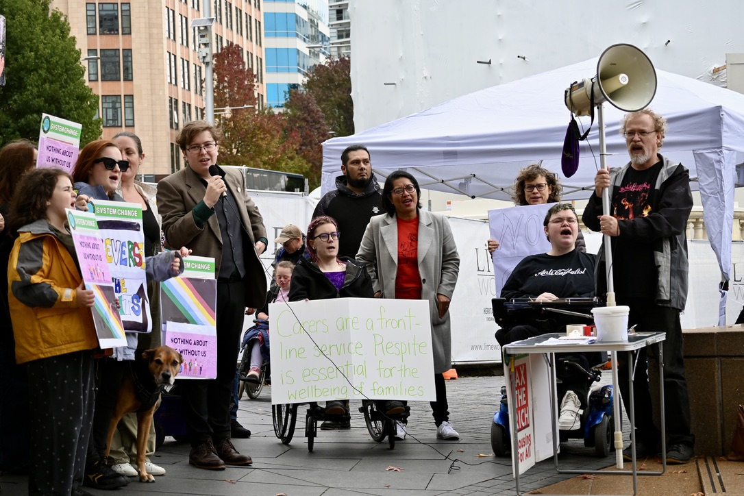 A crowd of disabled and nondisabled chant at a protest rally, a sign reads: Carers are a frontline service. Respite is essential for the welling of families.